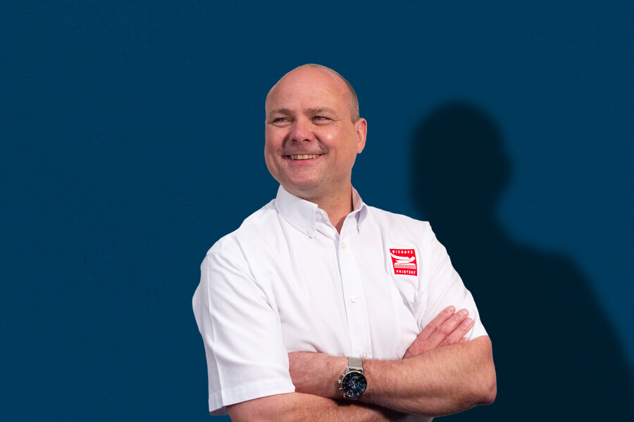 Paul Cull Production Director Paul Cull stood with his arms crossed in a white Bishops Printers shirt